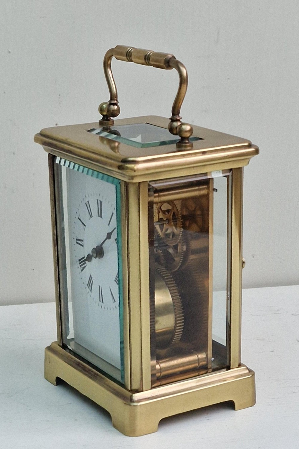 An antique French brass carriage clock featuring bevelled glass panels, a white enamel dial with black Roman numerals, and a top carrying handle. View V