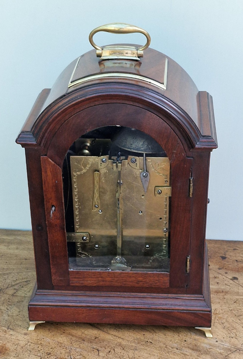 A Georgian mahogany bracket clock featuring an arched top with a brass carrying handle, silvered engraved dial with Roman numerals, and brass bracket feet. View IV