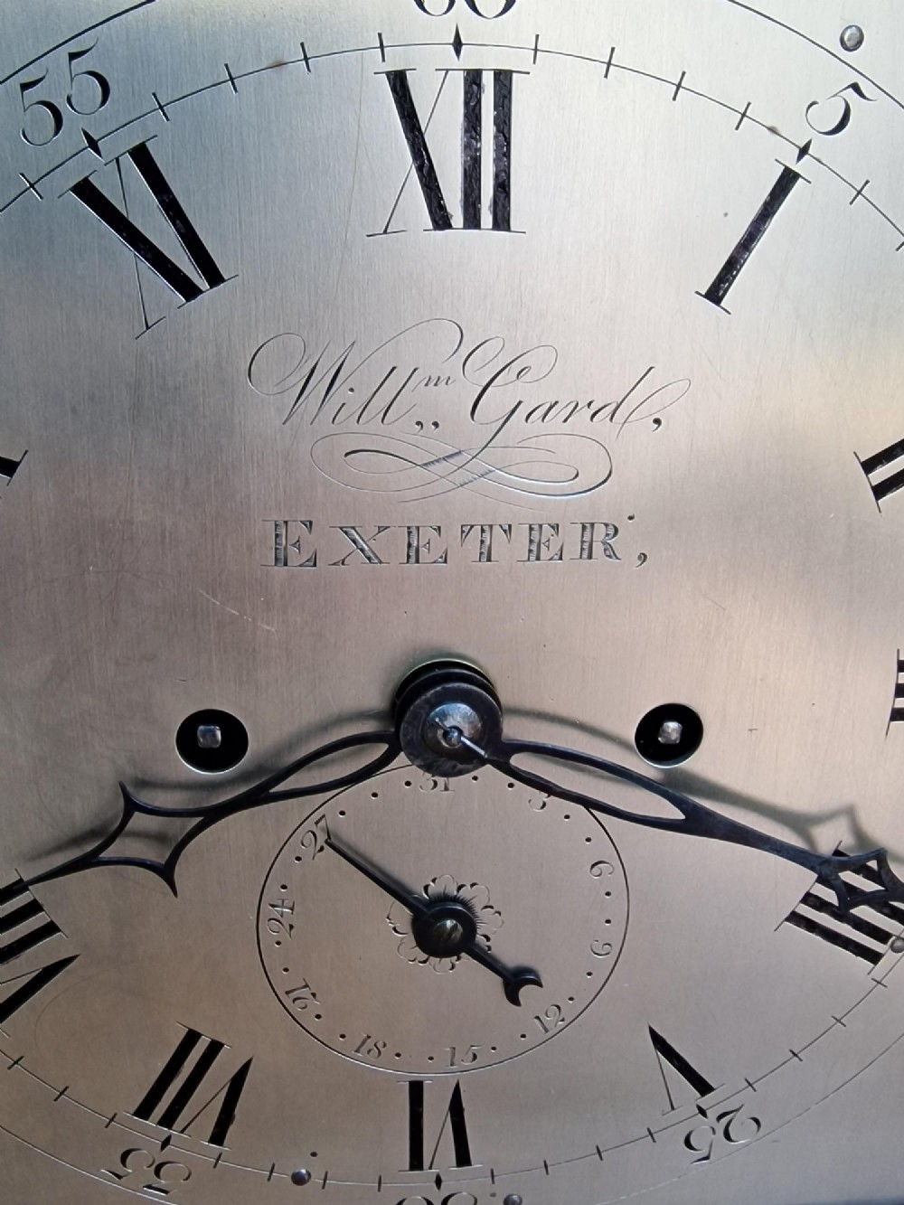 A Georgian mahogany bracket clock featuring an arched top with a brass carrying handle, silvered engraved dial with Roman numerals, and brass bracket feet. View V