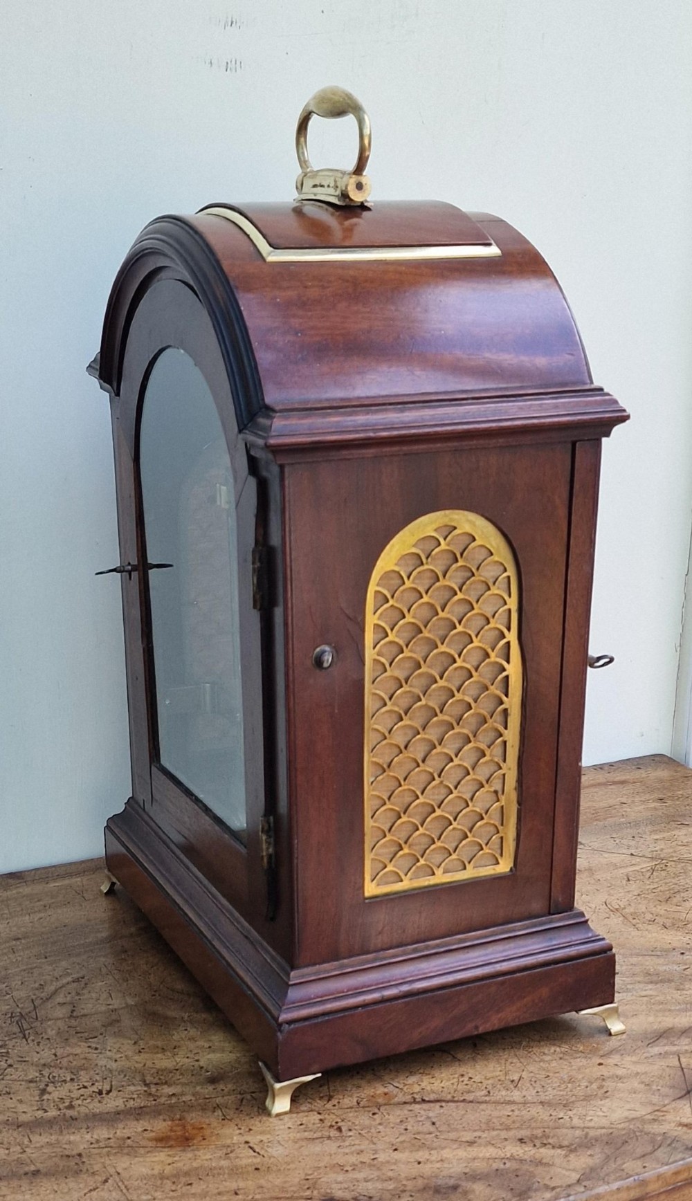 A Georgian mahogany bracket clock featuring an arched top with a brass carrying handle, silvered engraved dial with Roman numerals, and brass bracket feet. View VII