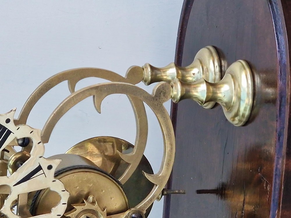 A Victorian brass skeleton clock with an exposed mechanical movement and top strike bell, housed under a clear glass dome on an oval mahogany base. View VII