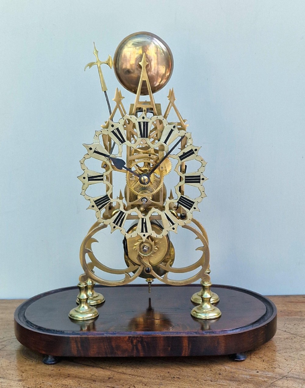 A Victorian brass skeleton clock with an exposed mechanical movement and top strike bell, housed under a clear glass dome on an oval mahogany base. View VIII