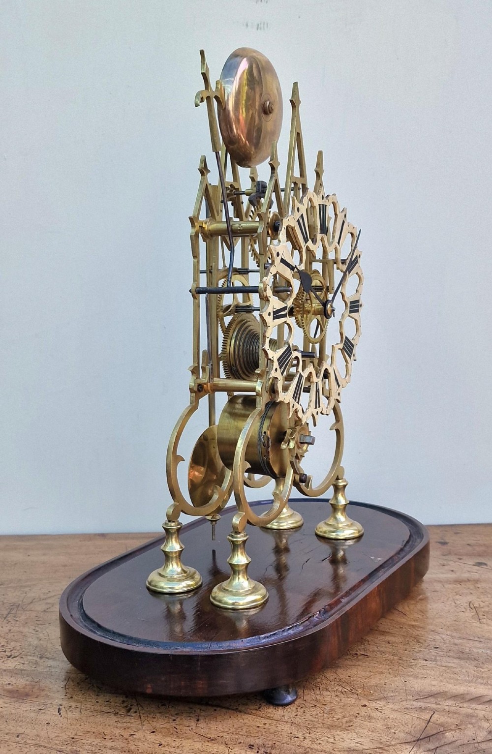 A Victorian brass skeleton clock with an exposed mechanical movement and top strike bell, housed under a clear glass dome on an oval mahogany base. View IX