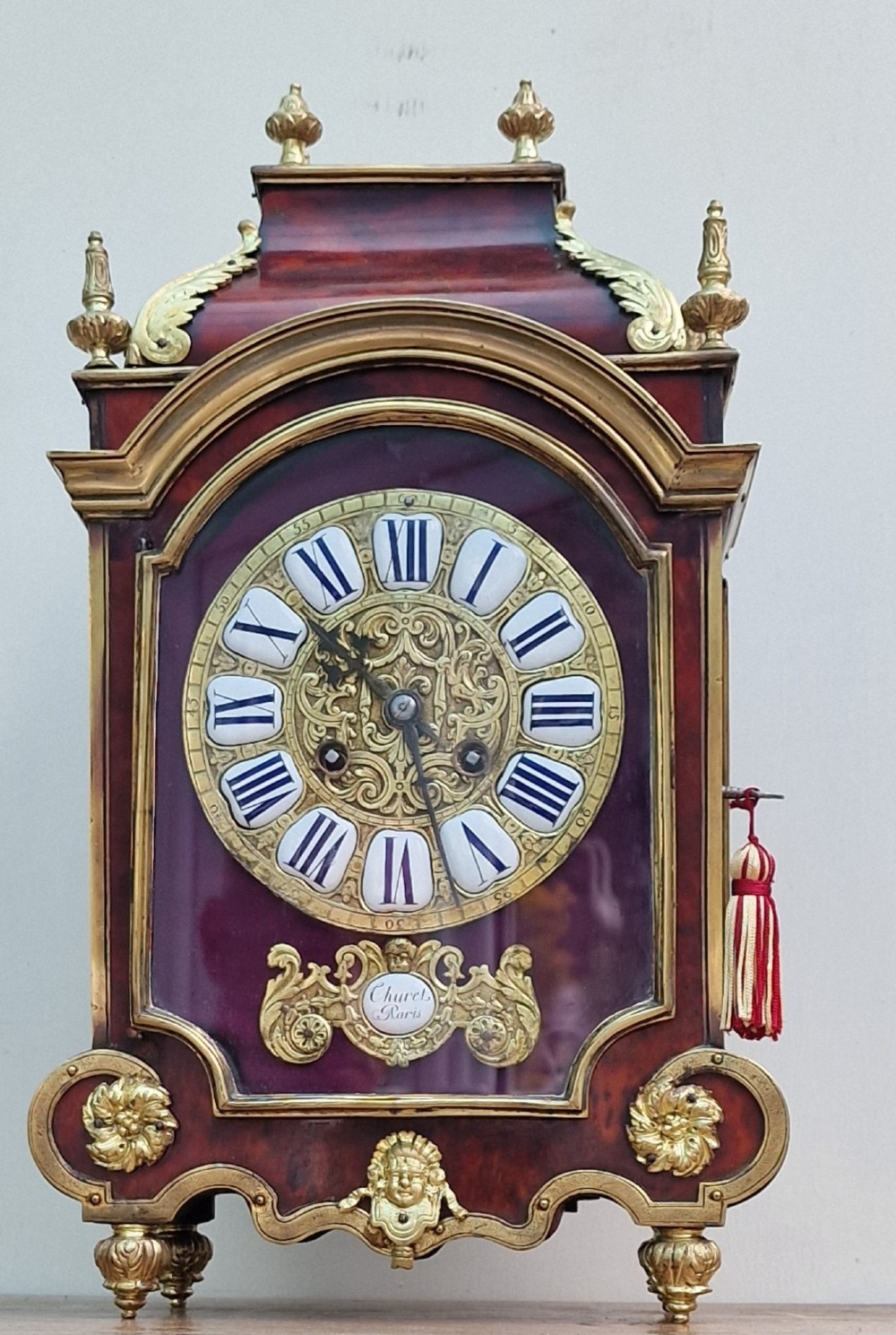 A red tortoiseshell and gilt bronze mantel clock featuring enamel Roman numeral cartouches and cast finials. View II