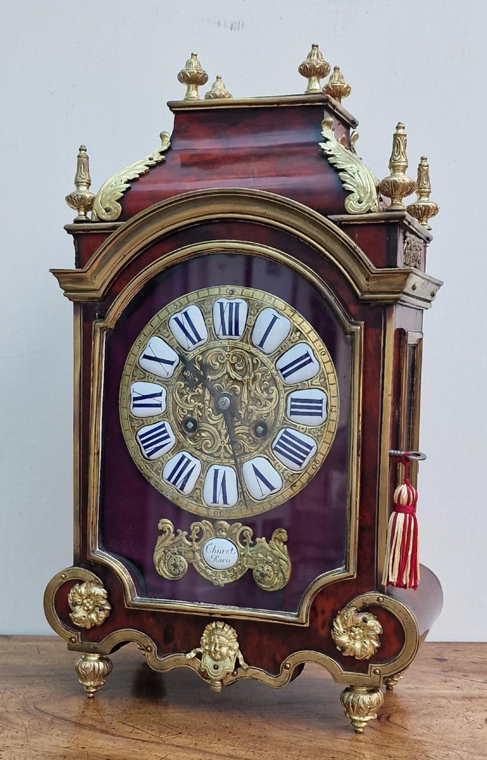 A red tortoiseshell and gilt bronze mantel clock featuring enamel Roman numeral cartouches and cast finials. View V