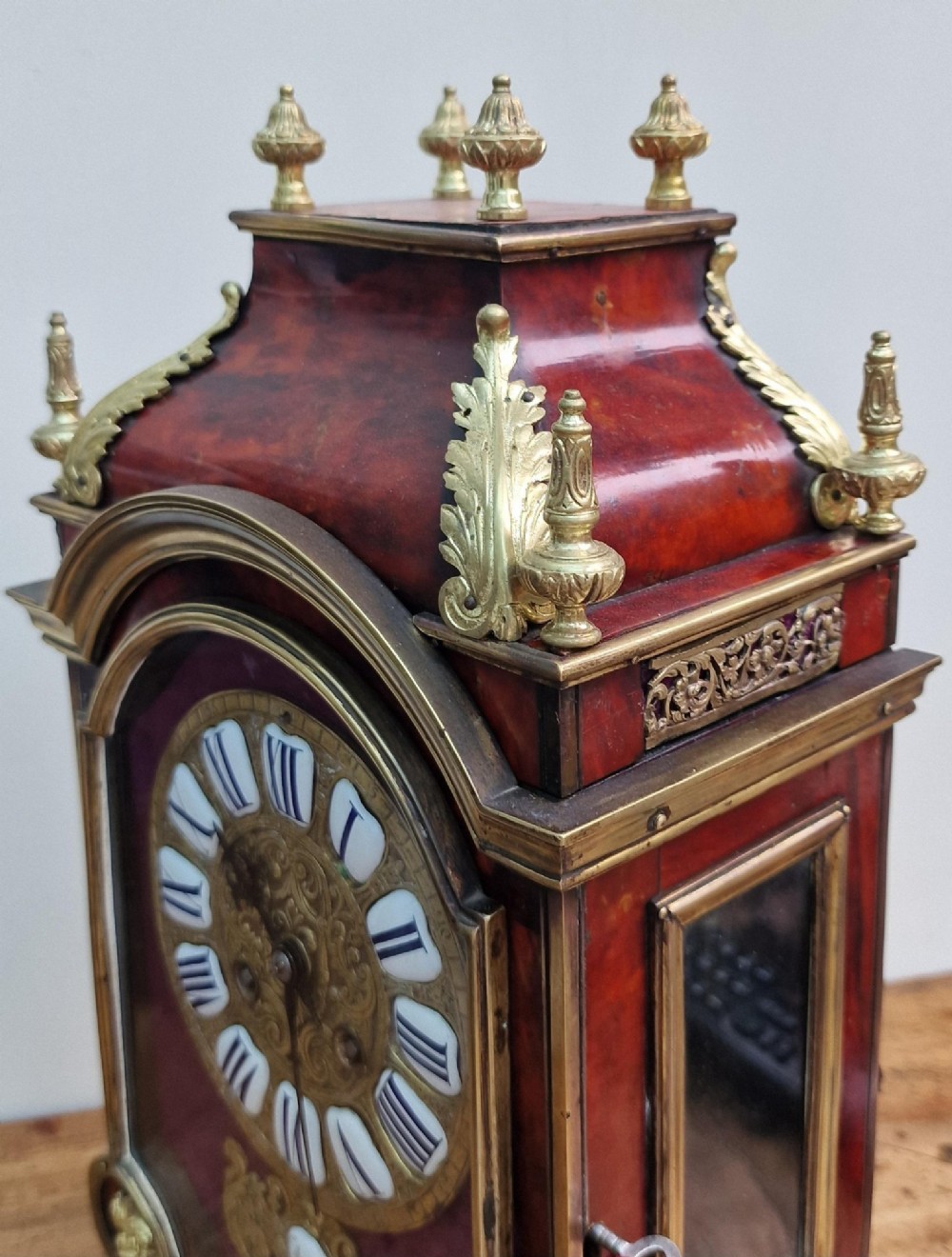 A red tortoiseshell and gilt bronze mantel clock featuring enamel Roman numeral cartouches and cast finials. View VIII