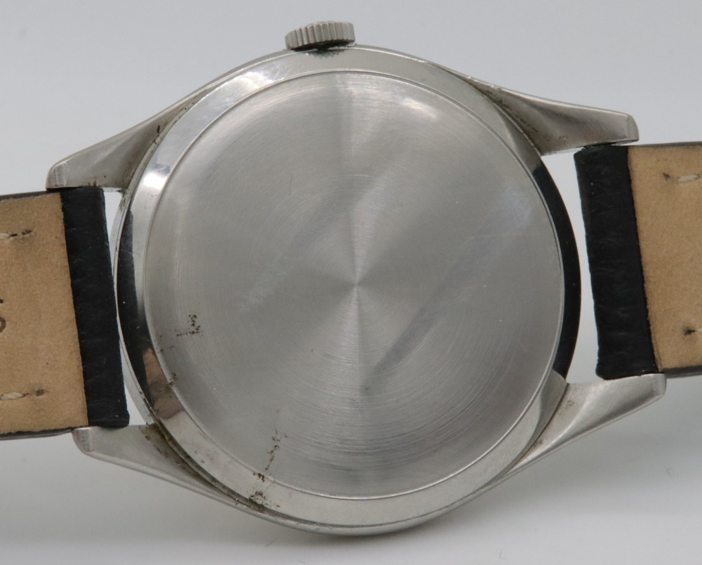 A 1947 Omega wristwatch featuring a circular stainless steel case, a patinated cream dial with Arabic numerals, a sub-seconds dial, and a black leather strap. View VI