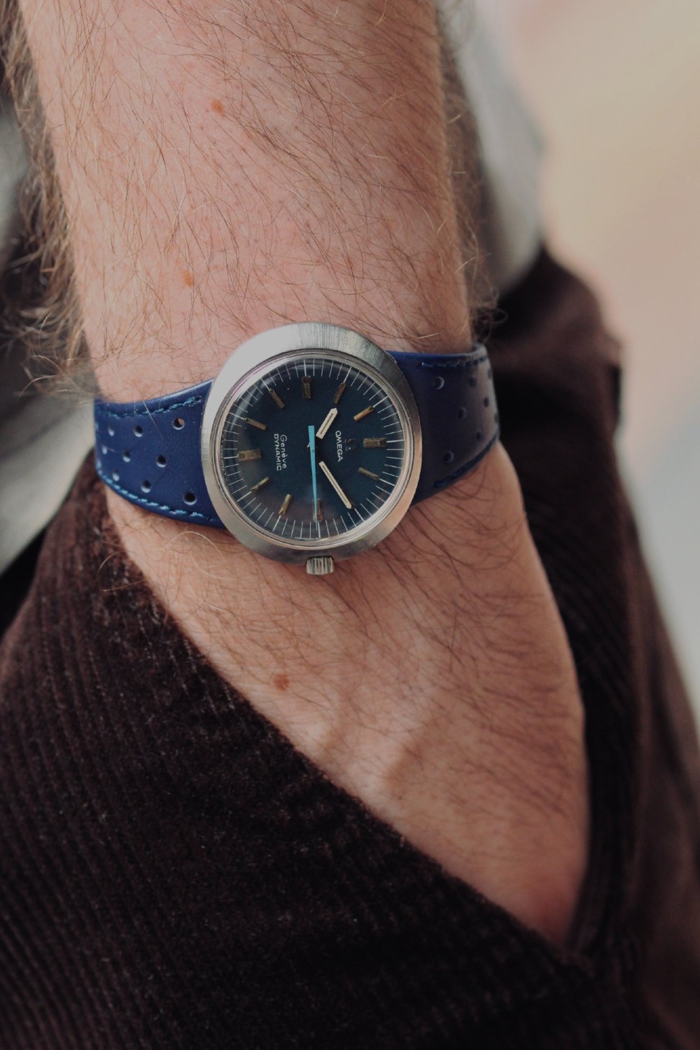 A 1969 Omega Geneve Dynamic stainless steel wristwatch with an elliptical case, dark navy dial, light blue seconds hand, and a perforated navy leather strap. View II