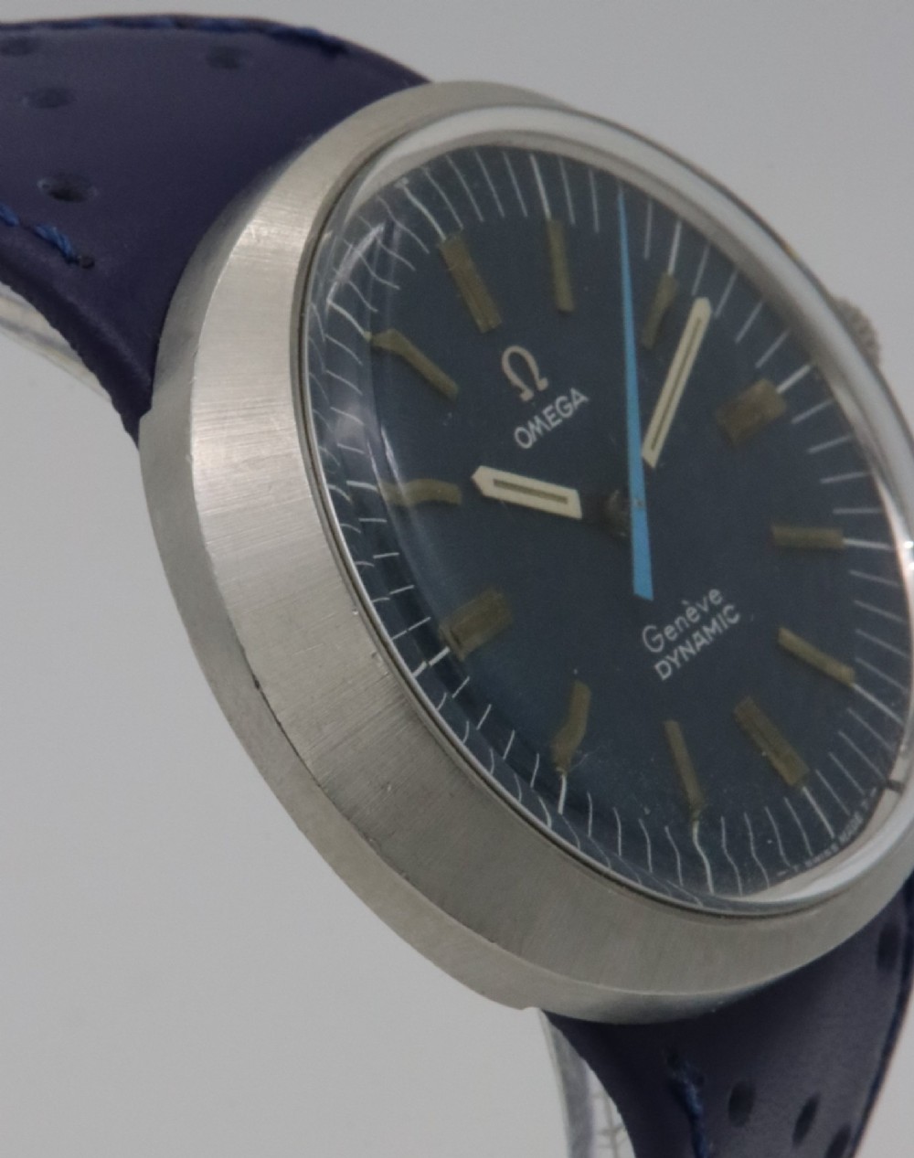 A 1969 Omega Geneve Dynamic stainless steel wristwatch with an elliptical case, dark navy dial, light blue seconds hand, and a perforated navy leather strap. View V