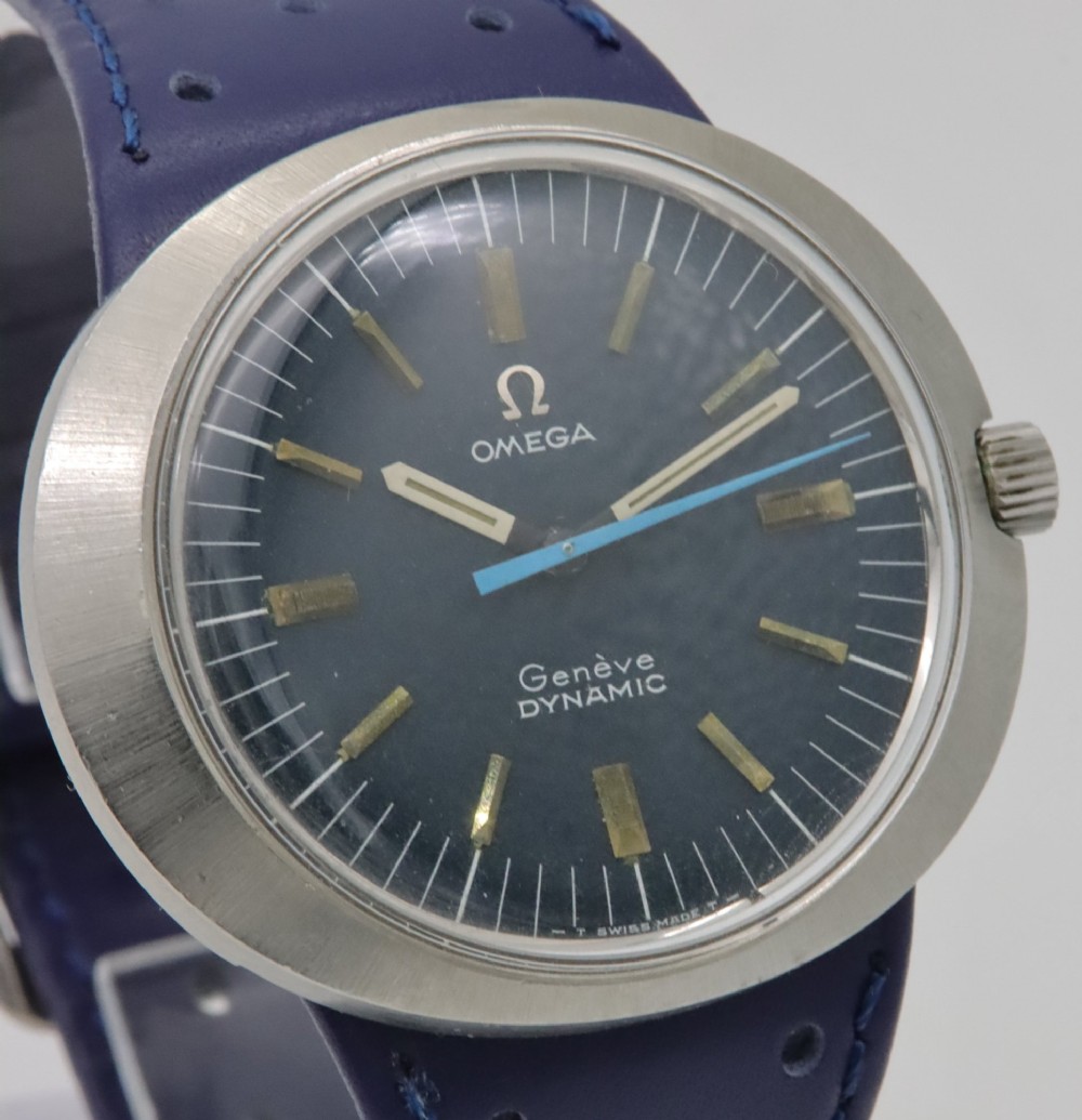 A 1969 Omega Geneve Dynamic stainless steel wristwatch with an elliptical case, dark navy dial, light blue seconds hand, and a perforated navy leather strap. View VI