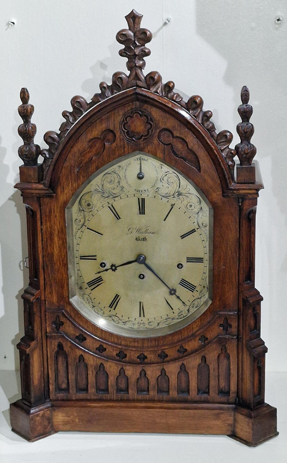 A carved oak Gothic Revival bracket clock featuring pointed arch cresting, turned finials, blind tracery details, and an engraved brass dial with Roman numerals. View II