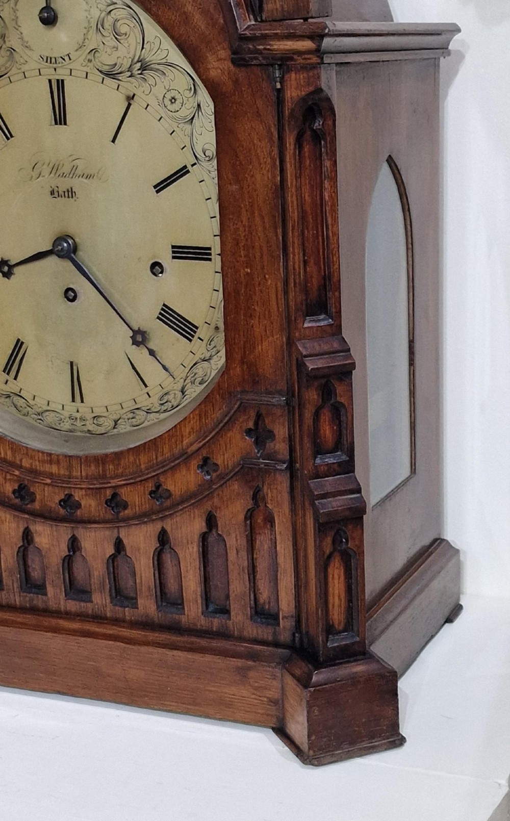 A carved oak Gothic Revival bracket clock featuring pointed arch cresting, turned finials, blind tracery details, and an engraved brass dial with Roman numerals. View V