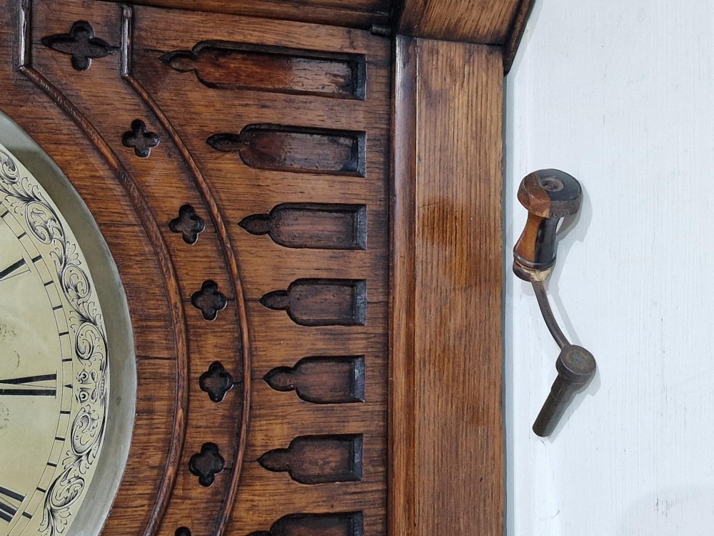 A carved oak Gothic Revival bracket clock featuring pointed arch cresting, turned finials, blind tracery details, and an engraved brass dial with Roman numerals. View VII
