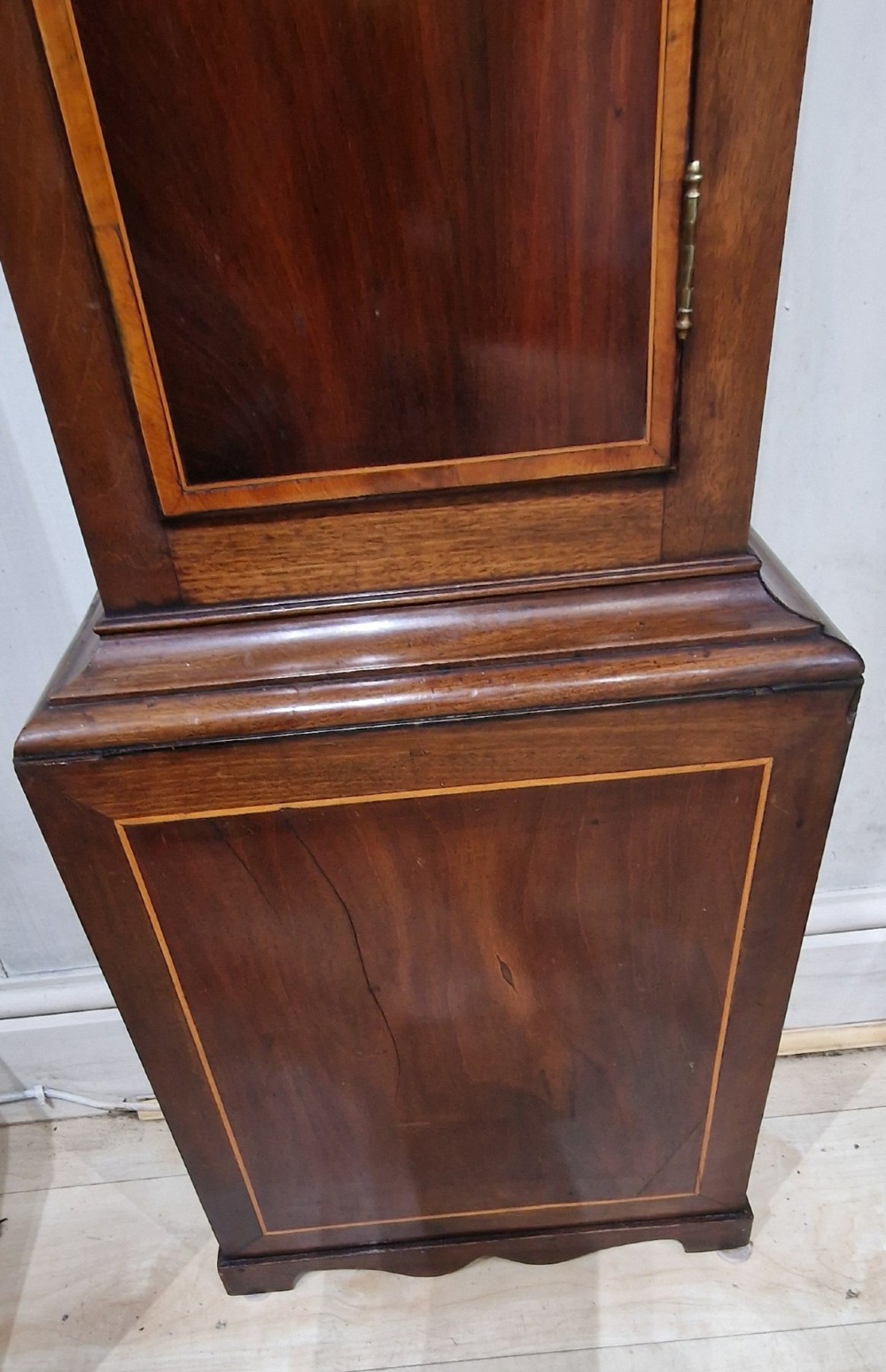 A Georgian mahogany grandmother clock featuring a swan-neck pediment, brass rosettes, an engraved brass and silvered dial, and an inlaid wooden trunk case. View II