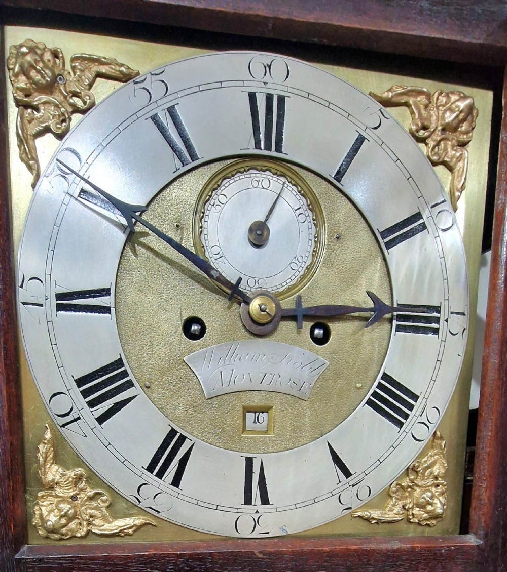 A Georgian mahogany grandmother clock featuring a swan-neck pediment, brass rosettes, an engraved brass and silvered dial, and an inlaid wooden trunk case. View III