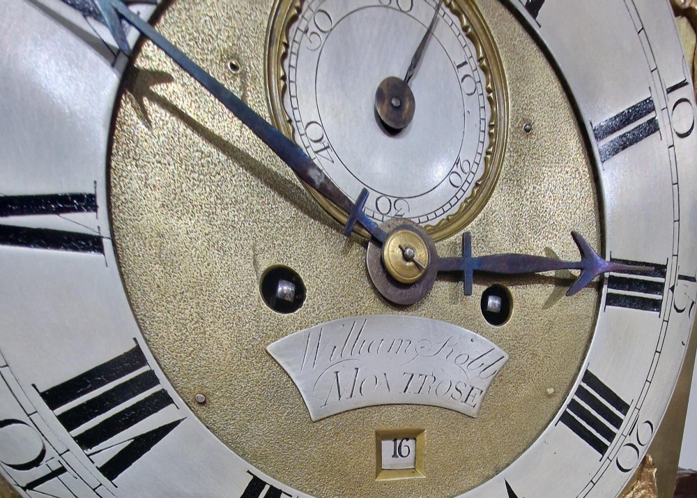 A Georgian mahogany grandmother clock featuring a swan-neck pediment, brass rosettes, an engraved brass and silvered dial, and an inlaid wooden trunk case. View VI