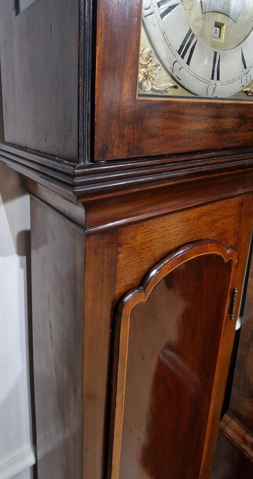 A Georgian mahogany grandmother clock featuring a swan-neck pediment, brass rosettes, an engraved brass and silvered dial, and an inlaid wooden trunk case. View VII