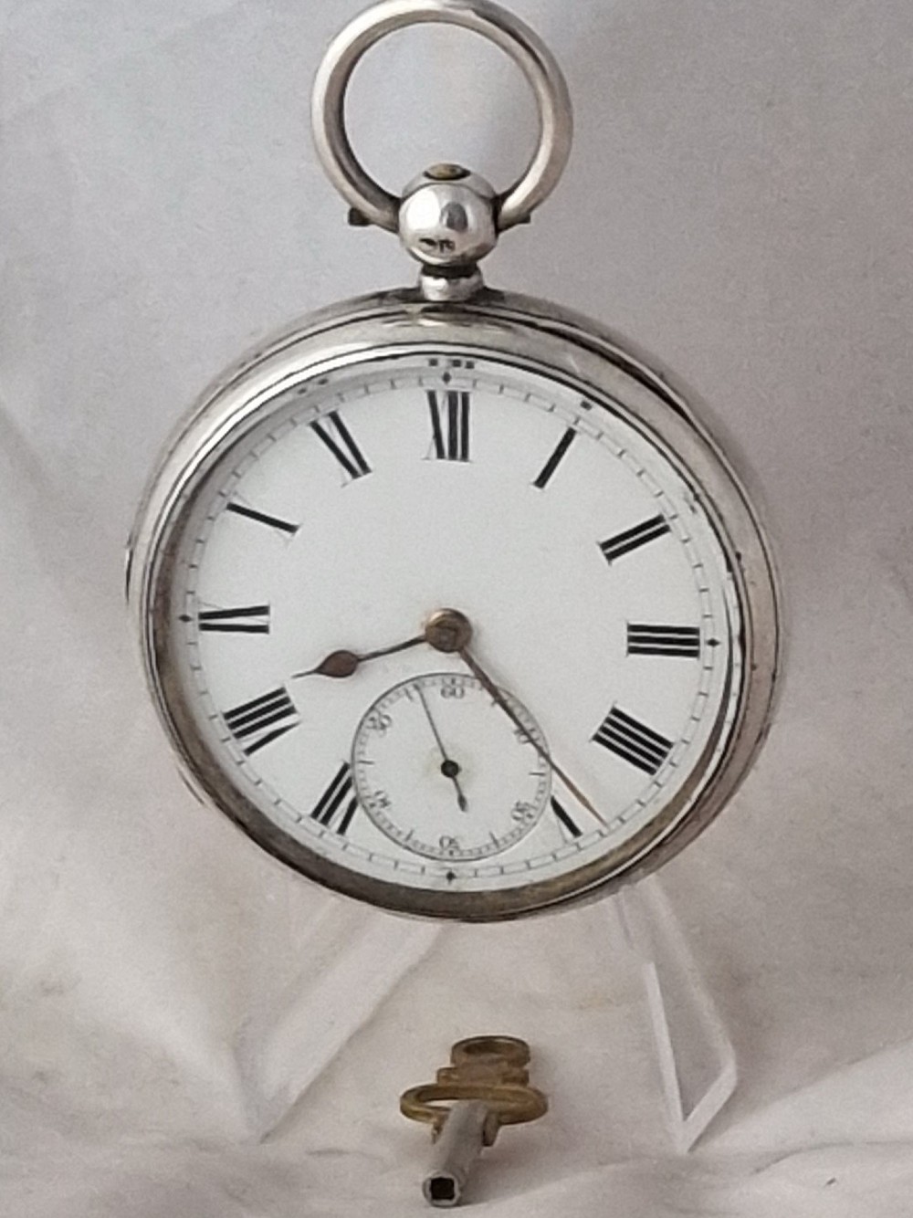 An antique silver open face fusee pocket watch featuring a white enamel dial with black Roman numerals, a subsidiary seconds dial, and an accompanying winding key.