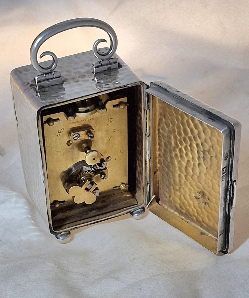 An Edwardian sterling silver carriage clock featuring a planished hammered case, scrolling carrying handle, ball feet, and a white dial with Roman numerals. View III
