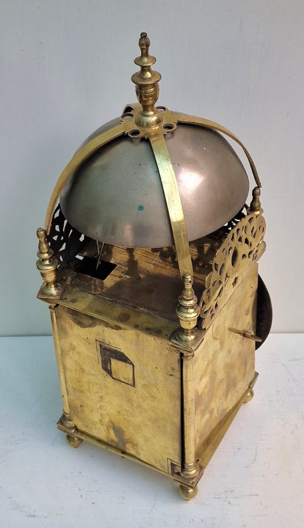 A 17th-century English brass lantern clock featuring an overhead bell, decorative pierced frets, ball feet, and an engraved dial centre signed Thomas Langley London. View II