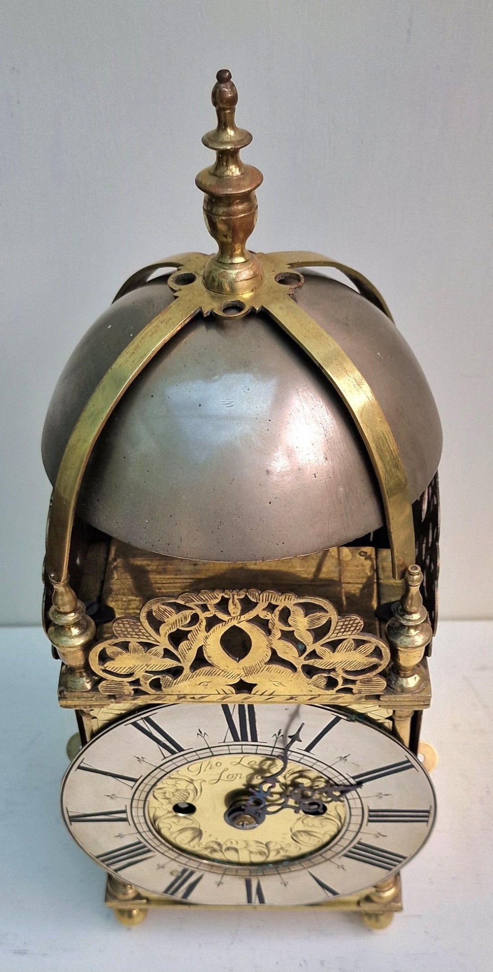 A 17th-century English brass lantern clock featuring an overhead bell, decorative pierced frets, ball feet, and an engraved dial centre signed Thomas Langley London. View VII