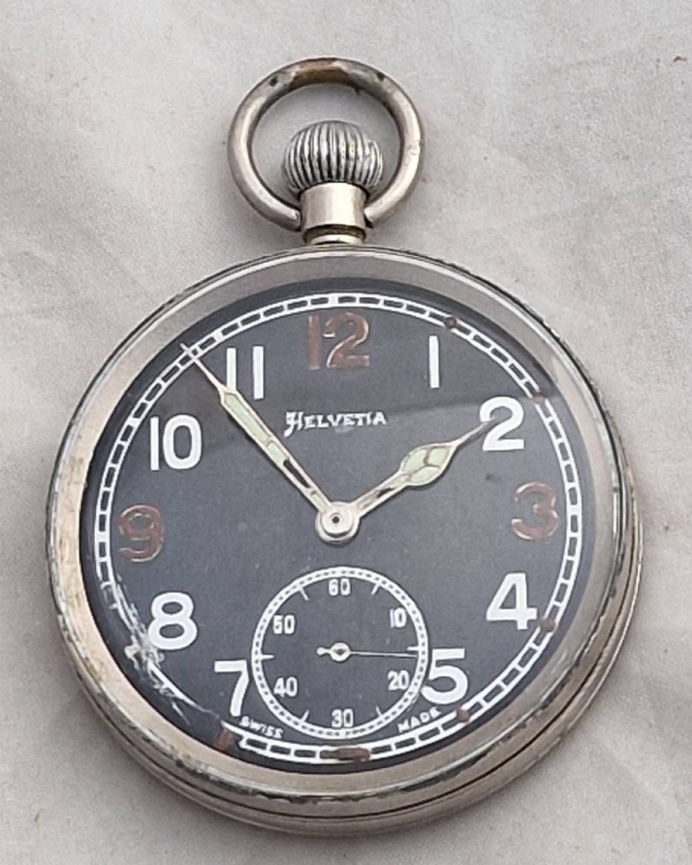 A Second World War Helvetia military pocket watch featuring a black dial with luminous Arabic numerals and a silver-toned metal case.