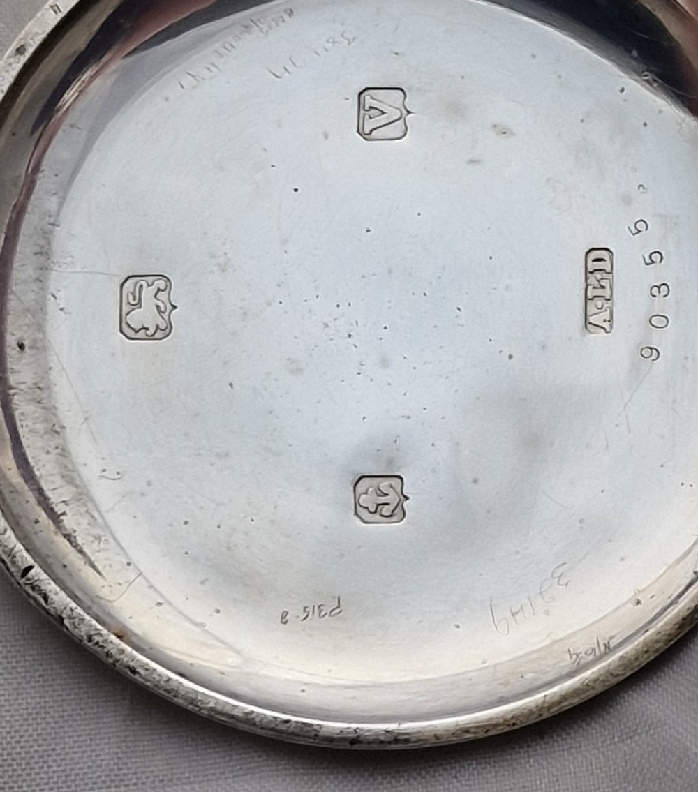 A polished silver half hunter pocket watch displaying an engraved outer ring with black Roman numerals surrounding a central circular glass window. View III