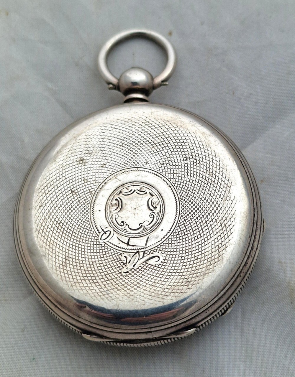 An open-face silver pocket watch displaying a white enamel dial with black Roman numerals, a subsidiary seconds dial, and an accompanying brass winding key. View II