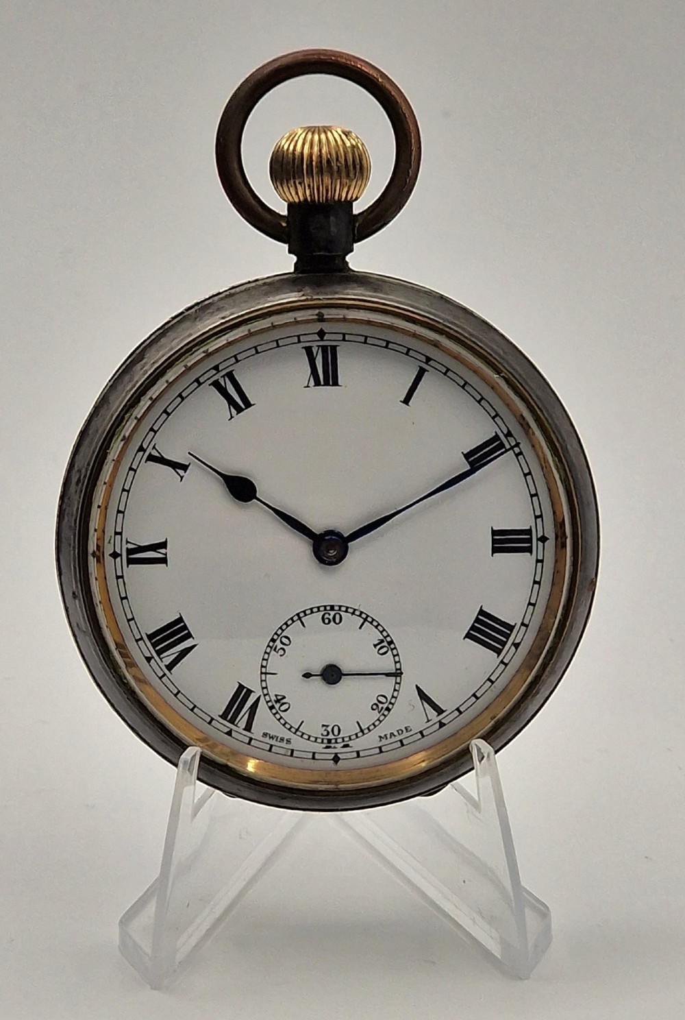 An open-face antique pocket watch with a white enamel dial, black Roman numerals, sub-seconds dial, and a silver metal case with a gold-toned crown.