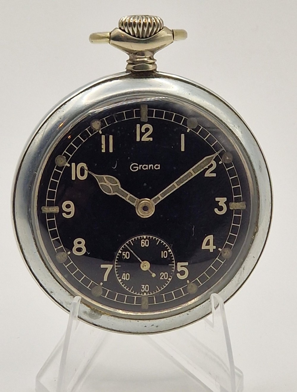 A vintage Grana military pocket watch with a silver-tone case, black dial, luminous Arabic numerals, and subsidiary seconds dial at six oclock.