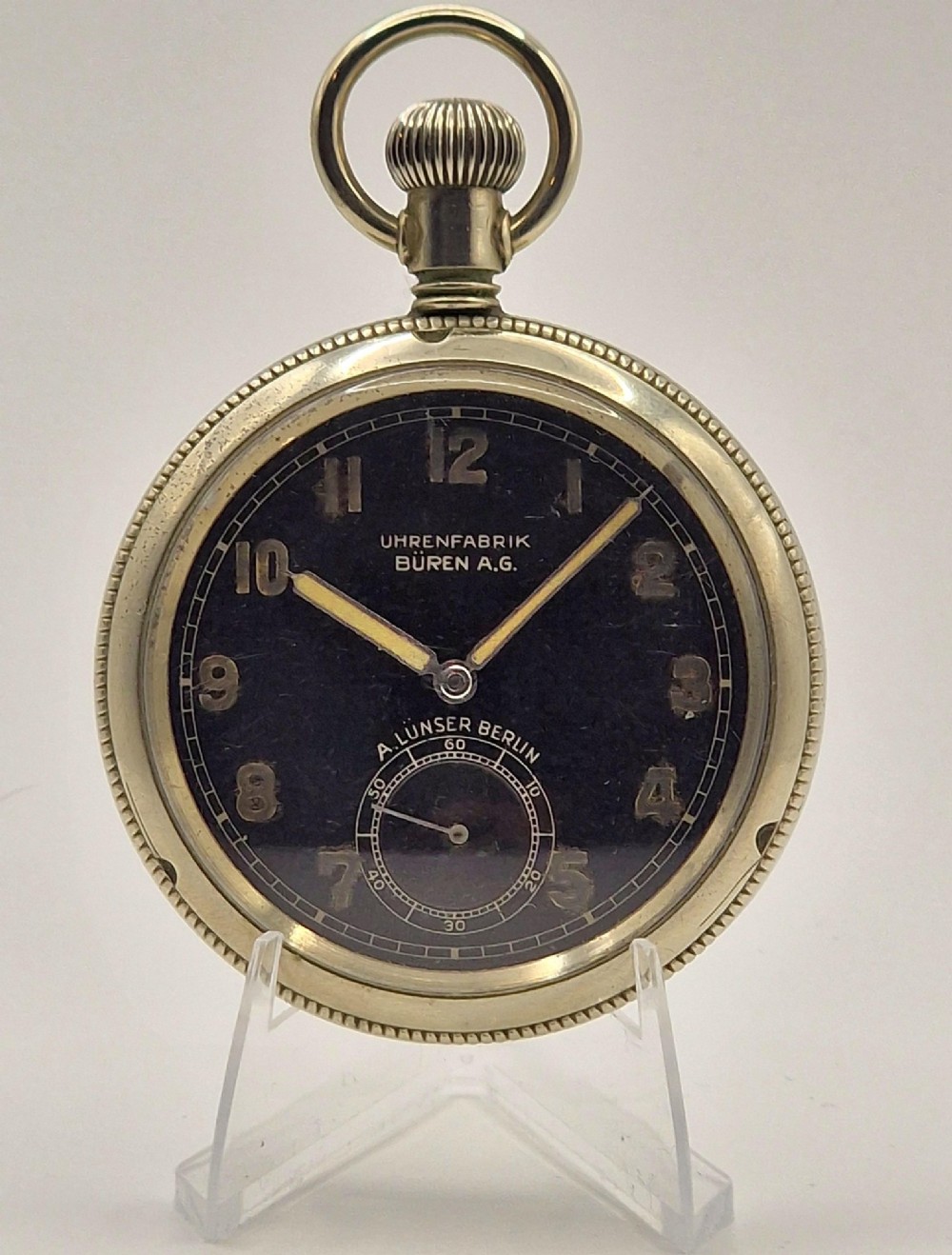 An open-face vintage military pocket watch featuring a black dial, Arabic numerals, luminous hands, a subsidiary seconds sub-dial, and a nickel case with top loop.
