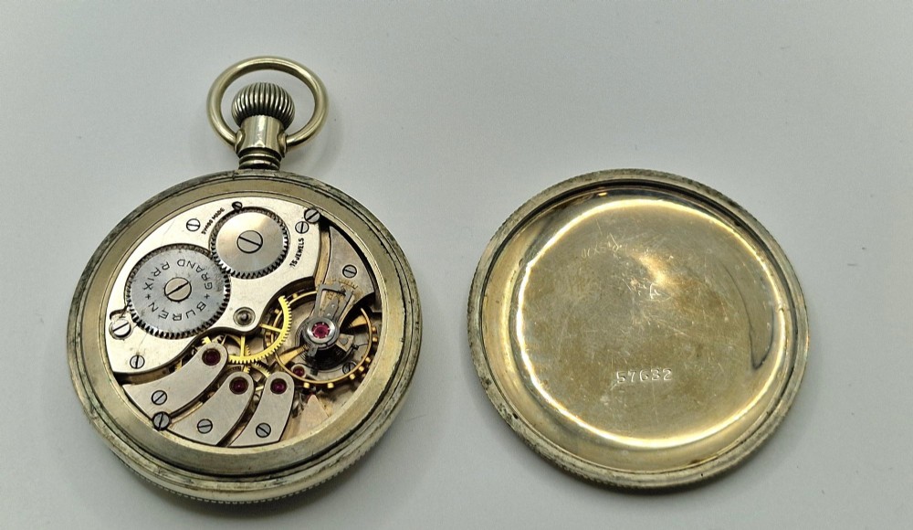 An open-face vintage military pocket watch featuring a black dial, Arabic numerals, luminous hands, a subsidiary seconds sub-dial, and a nickel case with top loop. View IV