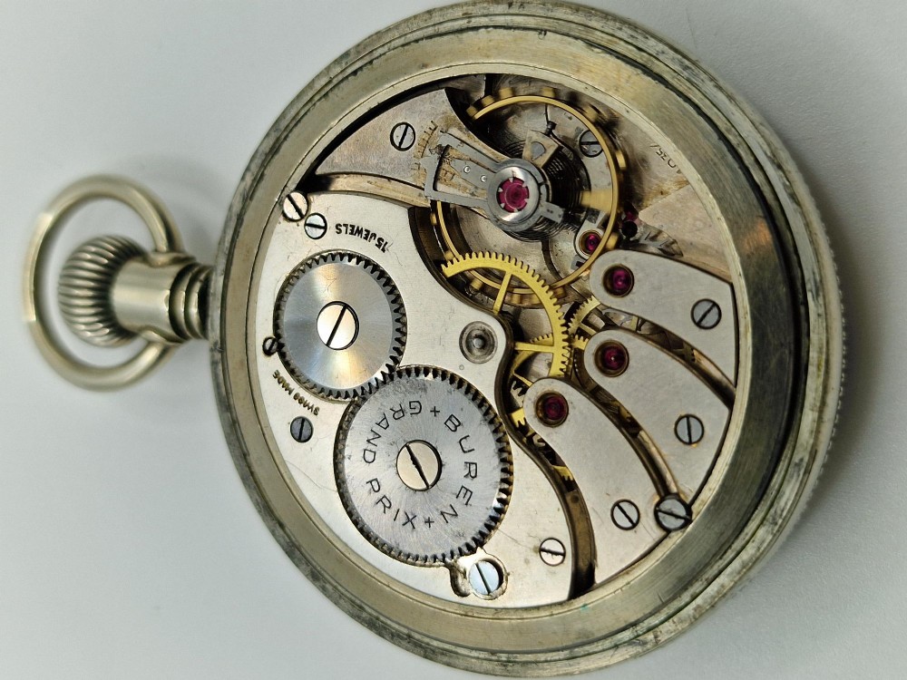 An open-face vintage military pocket watch featuring a black dial, Arabic numerals, luminous hands, a subsidiary seconds sub-dial, and a nickel case with top loop. View V