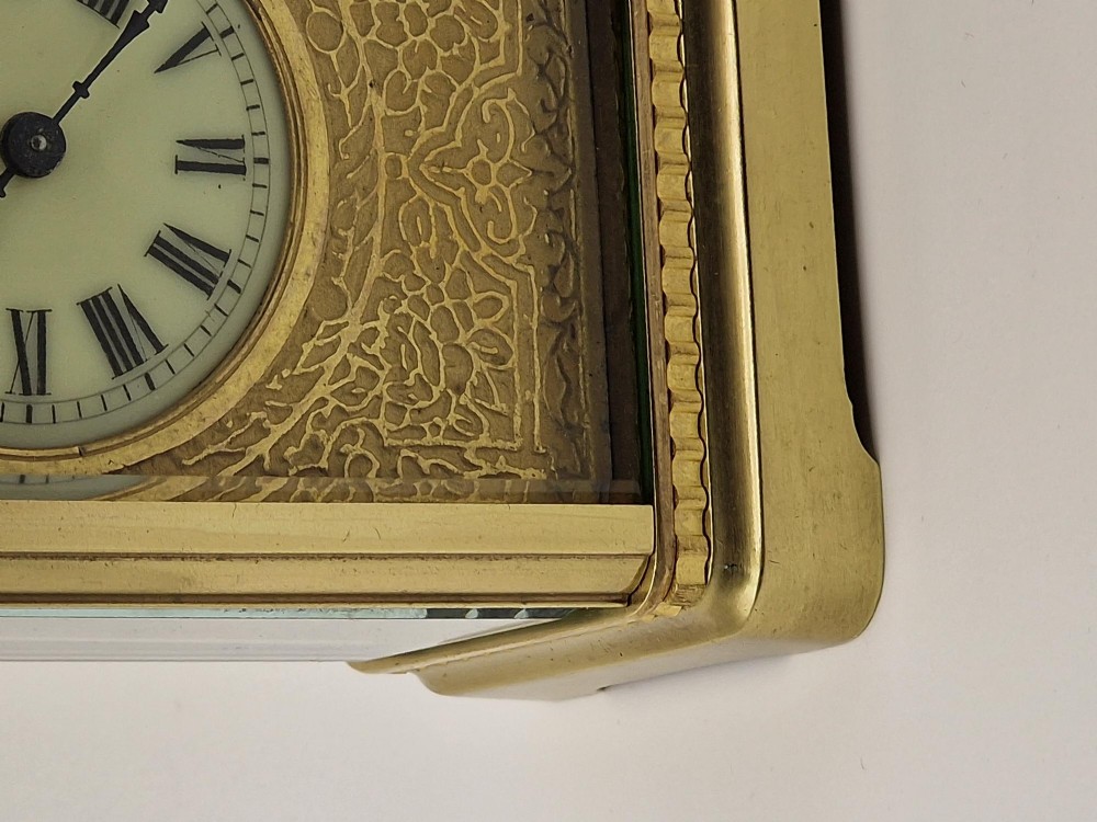 An antique brass carriage clock with an engraved gilded dial plate, white enamel face, and carrying handle, set next to its fitted brown leather transport case. View IV