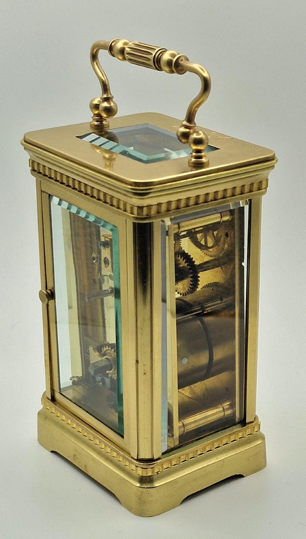 An antique brass carriage clock with an engraved gilded dial plate, white enamel face, and carrying handle, set next to its fitted brown leather transport case. View VIII