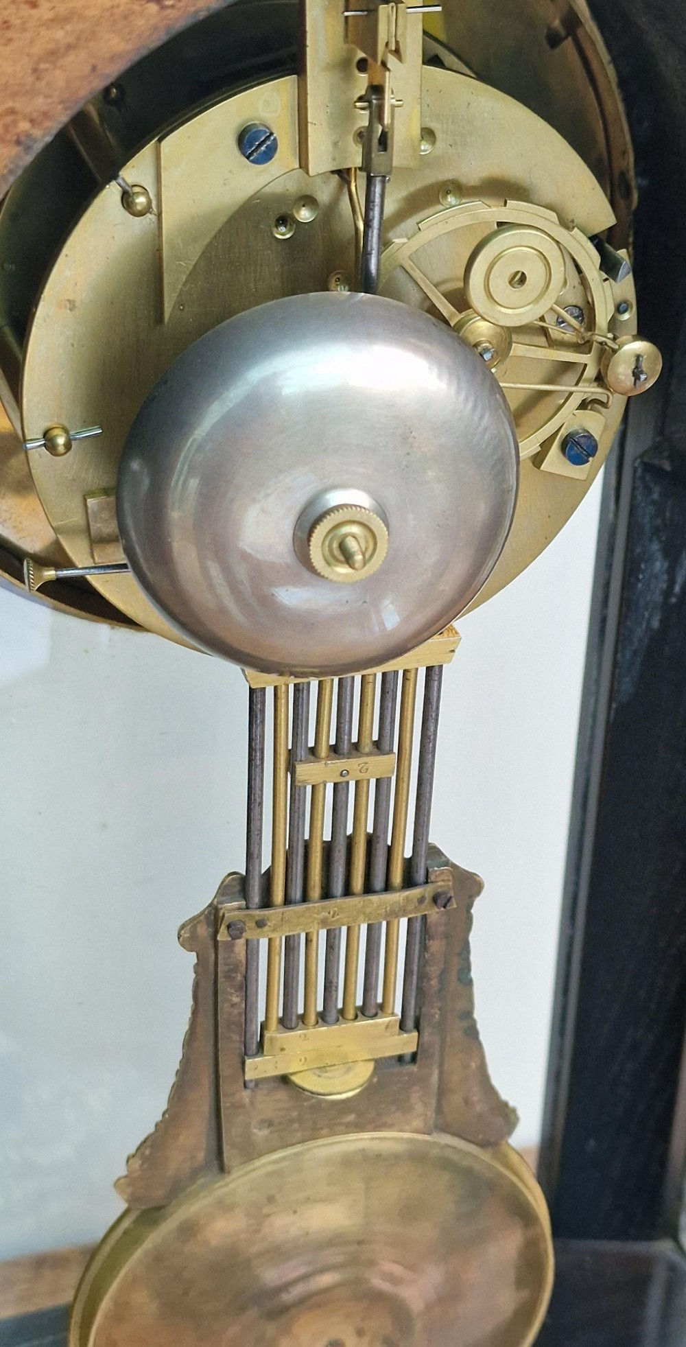An ebonised wooden mantel clock featuring floral brass and mother of pearl marquetry inlay, an arched glass front displaying a gridiron pendulum, and a white enamel dial with Roman numerals. View IV
