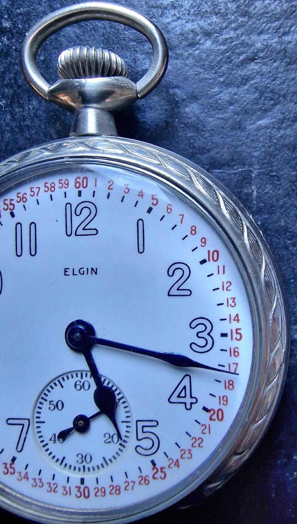 An open-face Elgin pocket watch with a white dial, black Arabic numerals, red outer minute markers, blued steel hands, and a silver-tone case. View III