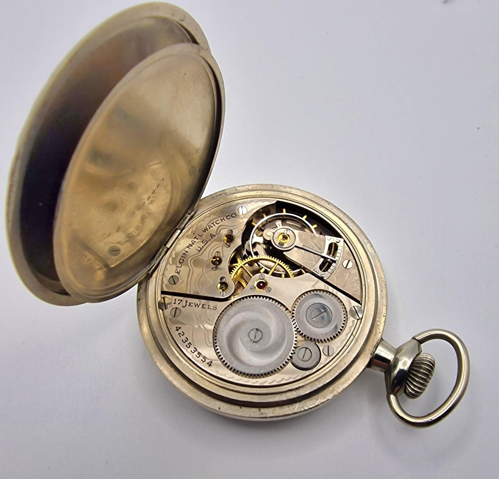 An open-face Elgin pocket watch with a white dial, black Arabic numerals, red outer minute markers, blued steel hands, and a silver-tone case. View V