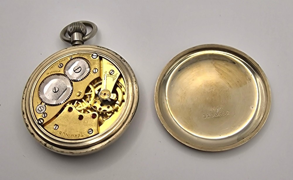 An open-face vintage Terminus military pocket watch featuring a white enamel dial with bold black Arabic numerals, a sub-seconds subdial at six oclock, and a reeded bezel. View III