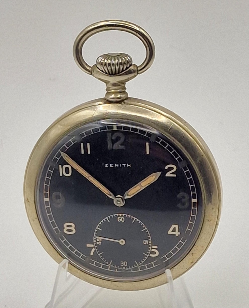 A Zenith open-face military pocket watch featuring a black dial, white Arabic numerals, a subsidiary seconds dial, and a silver-tone metal case.