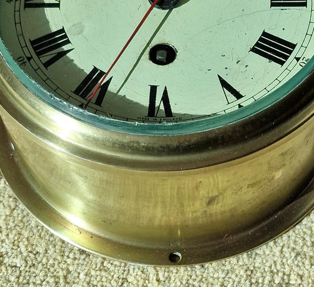 A circular brass Smiths Astral ships bulkhead clock with a white face, black Roman numerals, and a red second hand. View II