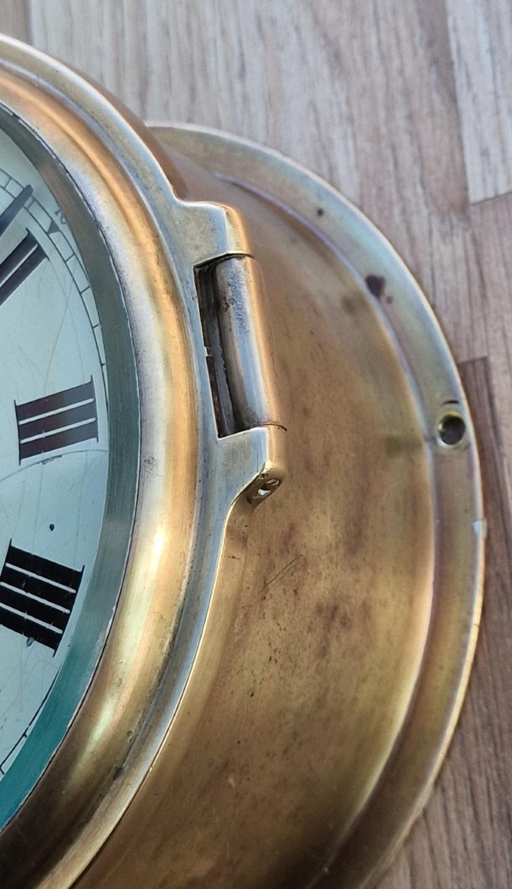 A circular brass Smiths Astral ships bulkhead clock with a white face, black Roman numerals, and a red second hand. View IV
