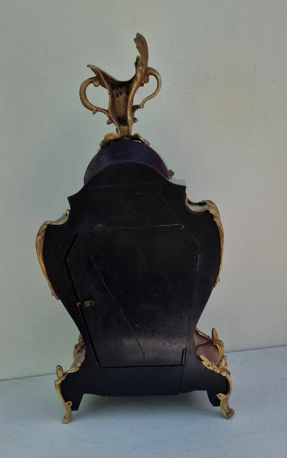 A French Rococo style mantel clock with a dark veneered balloon-shaped case, ornamental gilt-bronze foliage mounts, and a brass-rimmed dial showing Roman numerals. View II