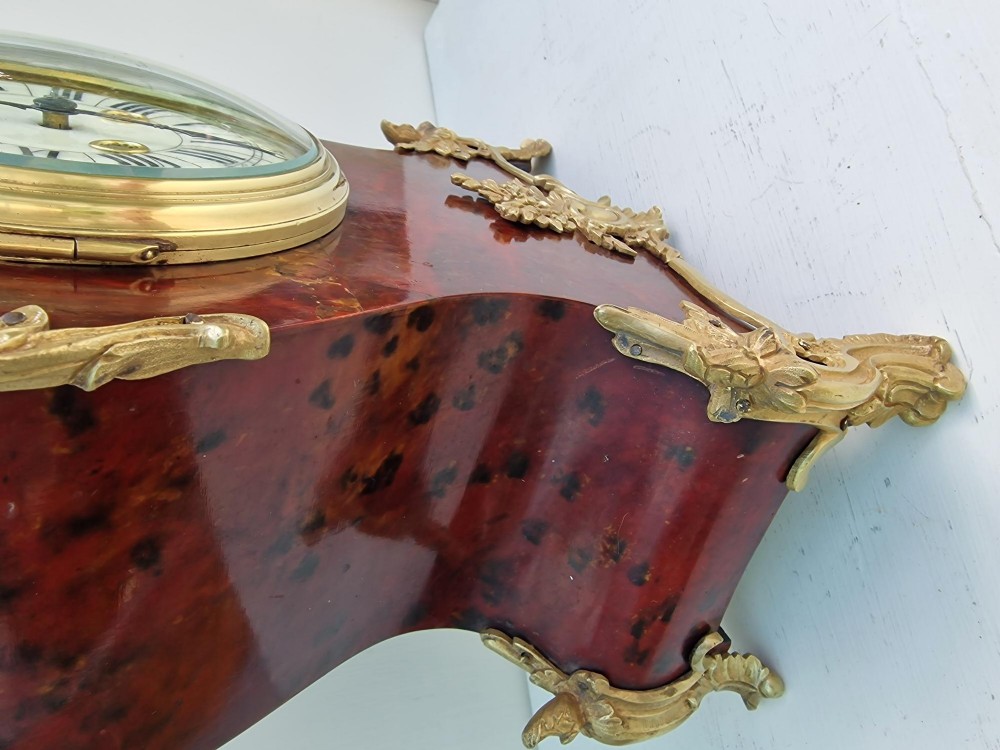 A French Rococo style mantel clock with a dark veneered balloon-shaped case, ornamental gilt-bronze foliage mounts, and a brass-rimmed dial showing Roman numerals. View V
