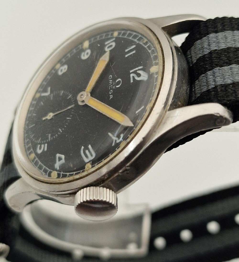 A vintage 1945 Omega military wristwatch featuring a stainless steel case, black dial with luminous Arabic numerals, sub-seconds dial, and a black and grey striped fabric strap. View VI
