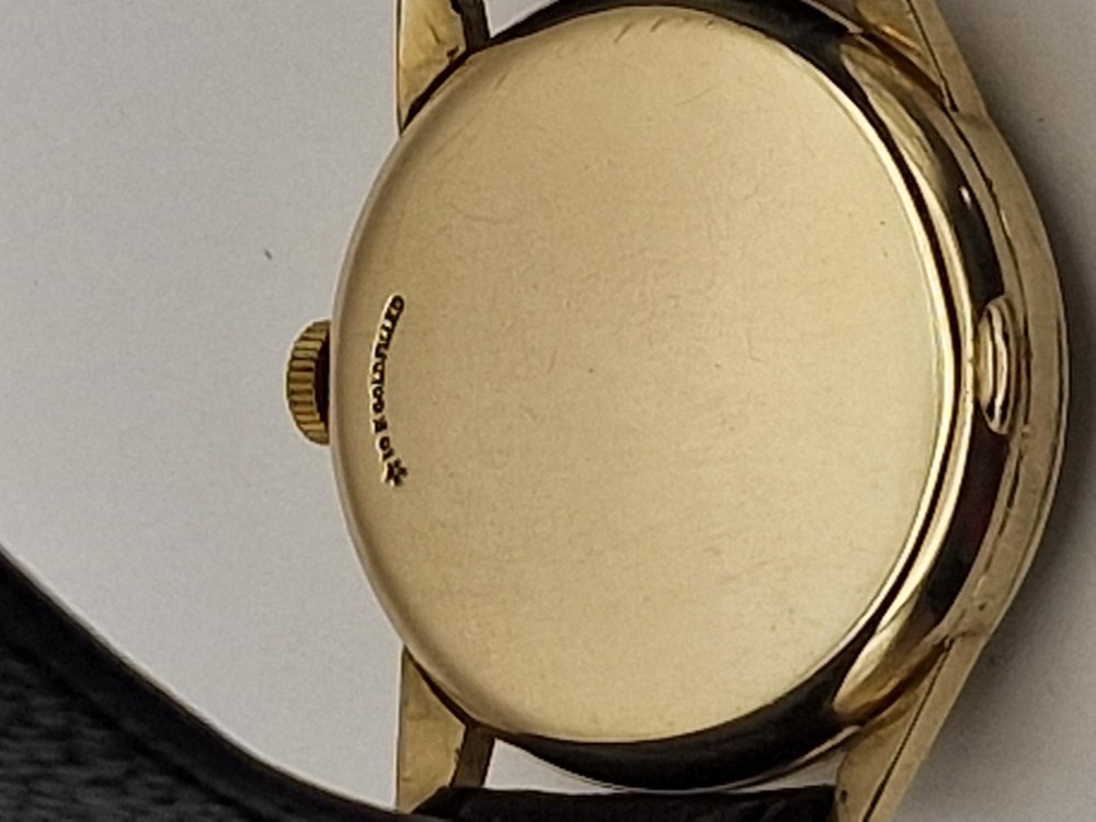 A 1954 Omega Century wristwatch with a gold-filled circular case, patinated dial with arrow markers, sub-seconds display, and a black leather strap. View II