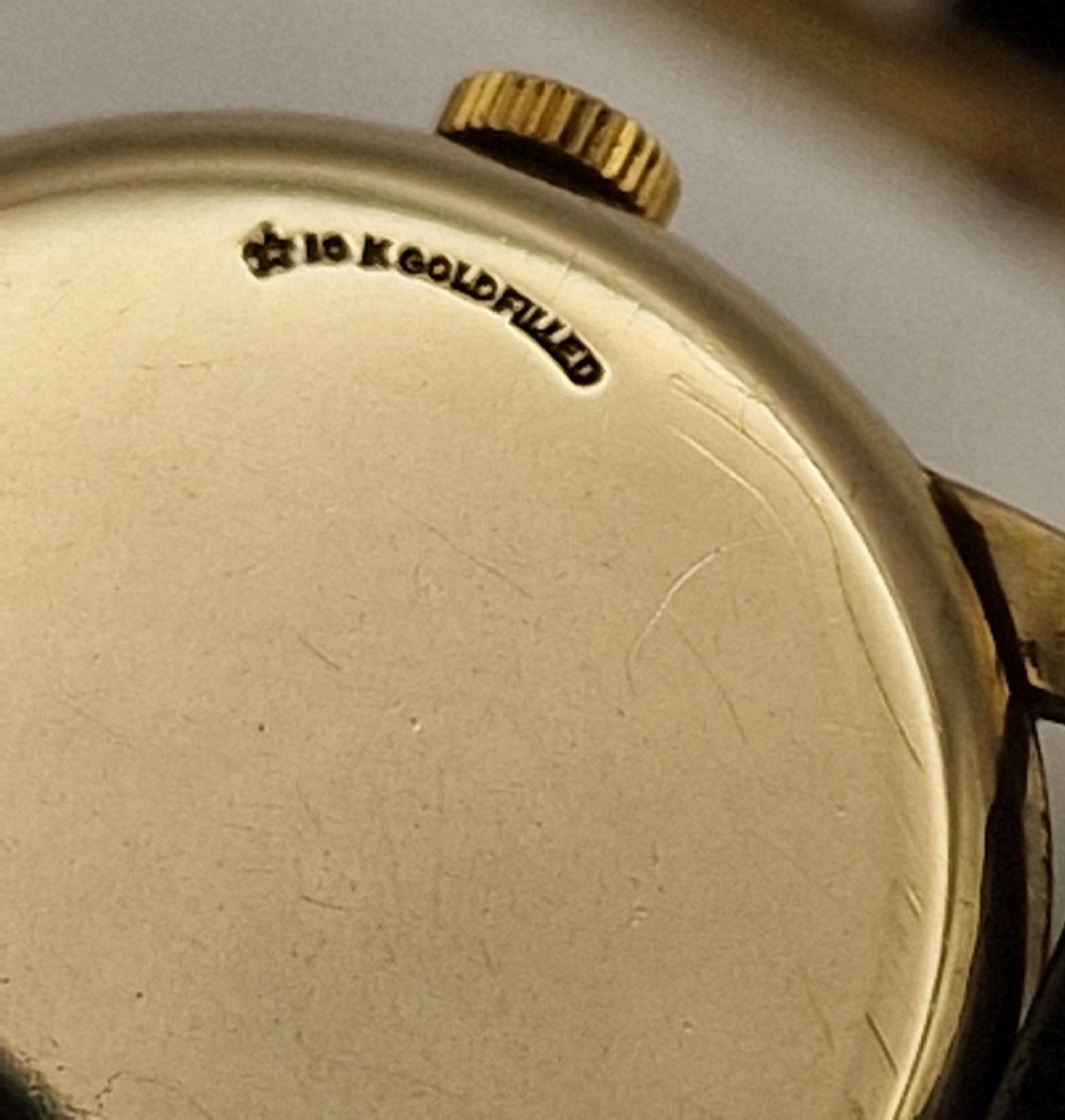 A 1954 Omega Century wristwatch with a gold-filled circular case, patinated dial with arrow markers, sub-seconds display, and a black leather strap. View IV
