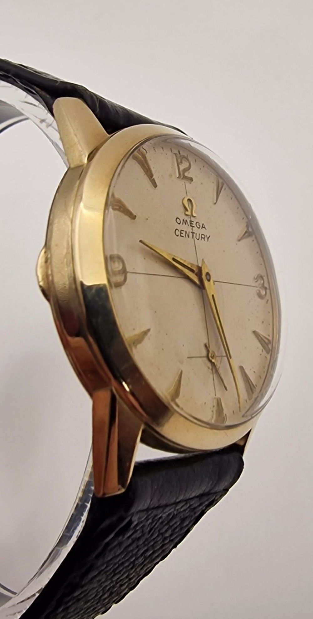 A 1954 Omega Century wristwatch with a gold-filled circular case, patinated dial with arrow markers, sub-seconds display, and a black leather strap. View V