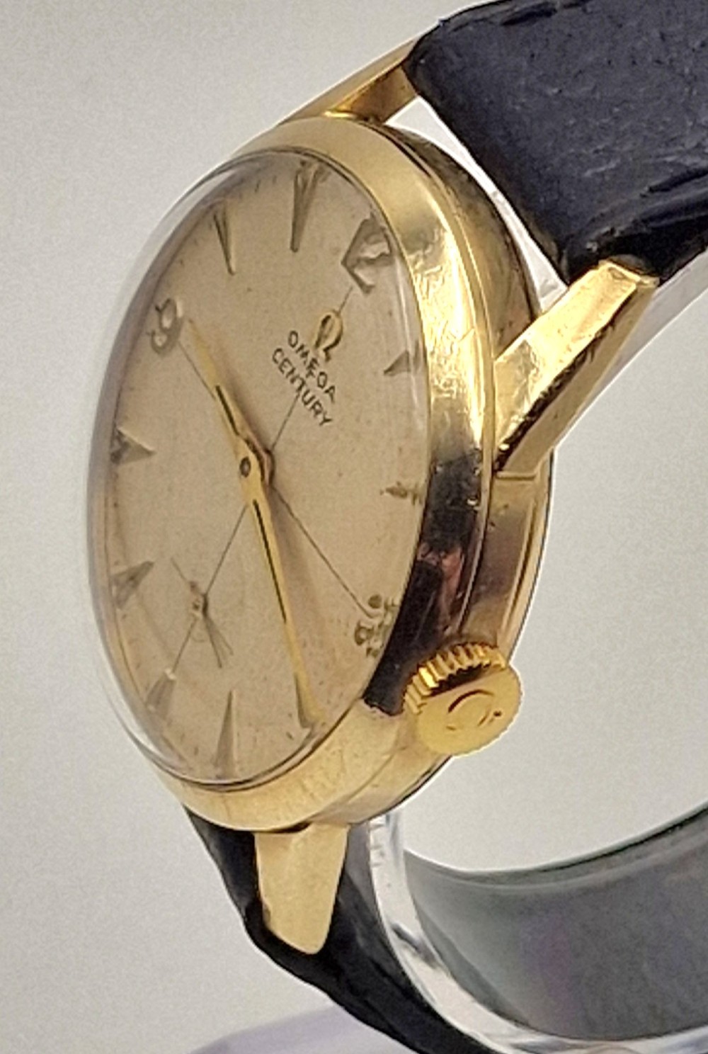 A 1954 Omega Century wristwatch with a gold-filled circular case, patinated dial with arrow markers, sub-seconds display, and a black leather strap. View VI