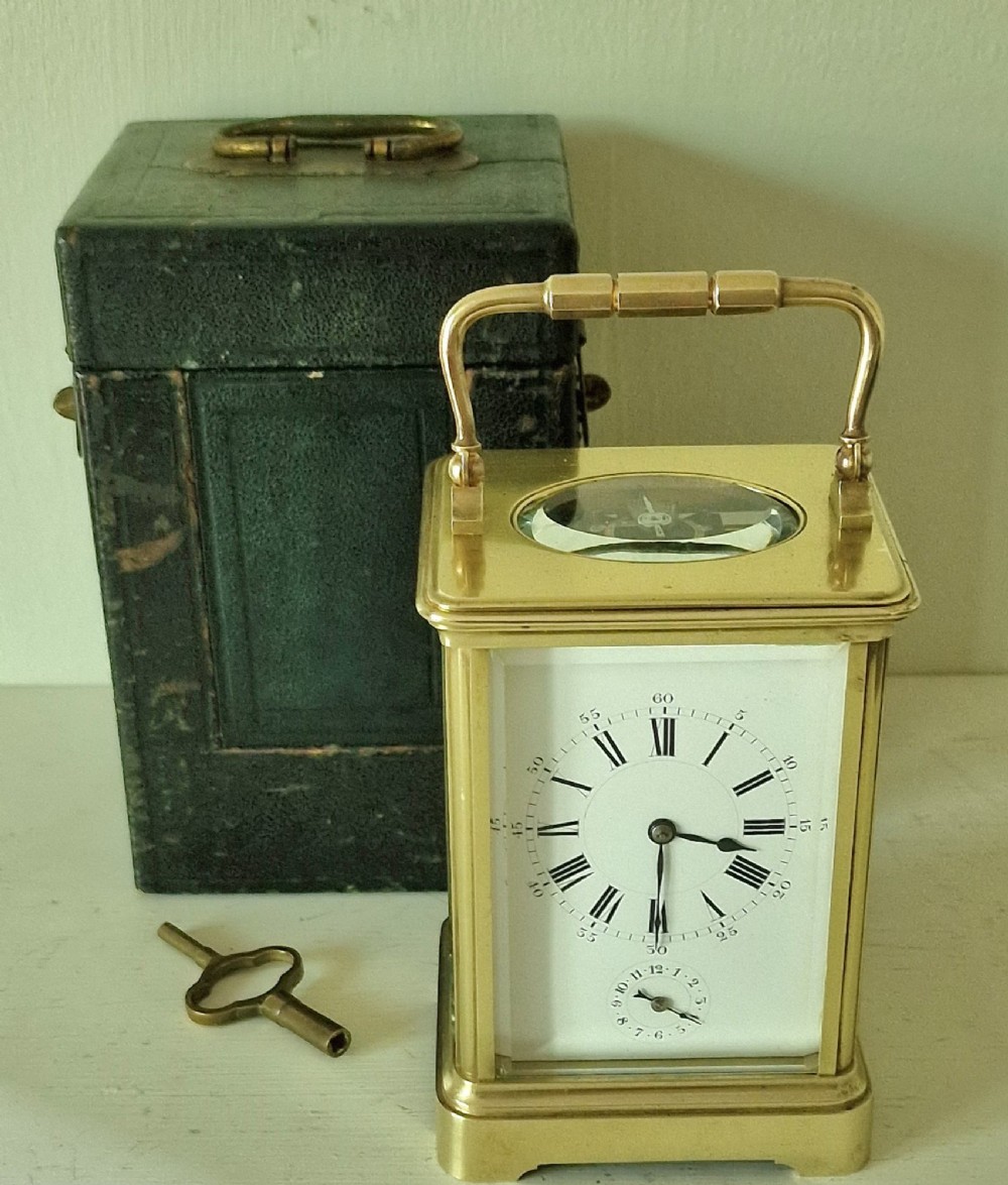 A French brass carriage clock with a top carrying handle, white enamel dial with Roman numerals, and clear glass side panels.